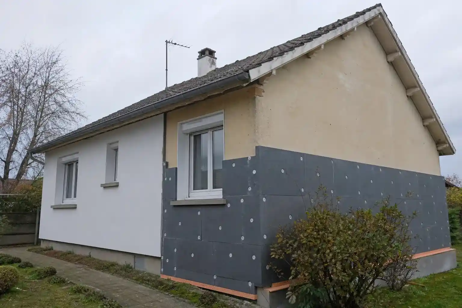 Façade de pavillon des années 80 en cours d’isolation par l’extérieur, panneaux isolants posés à mi-hauteur, finition enduit clair déjà visible sur une moitié