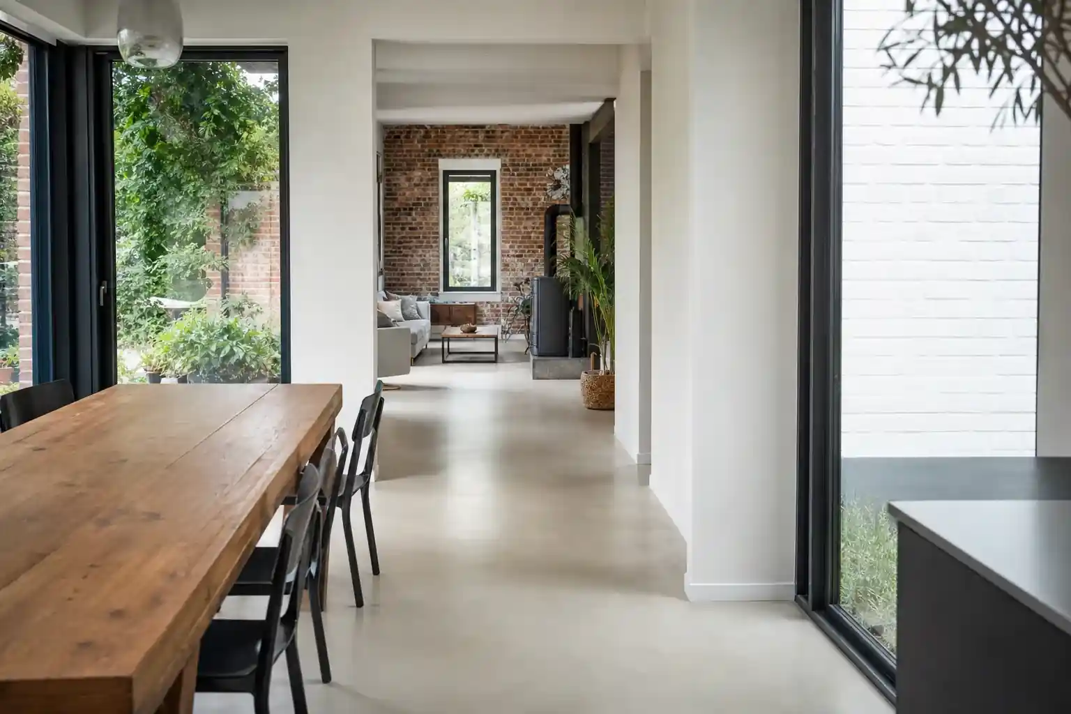 Intérieur d’une extension lumineuse, sol béton ciré, vue traversante vers l’ancien séjour en brique, mobilier sobre