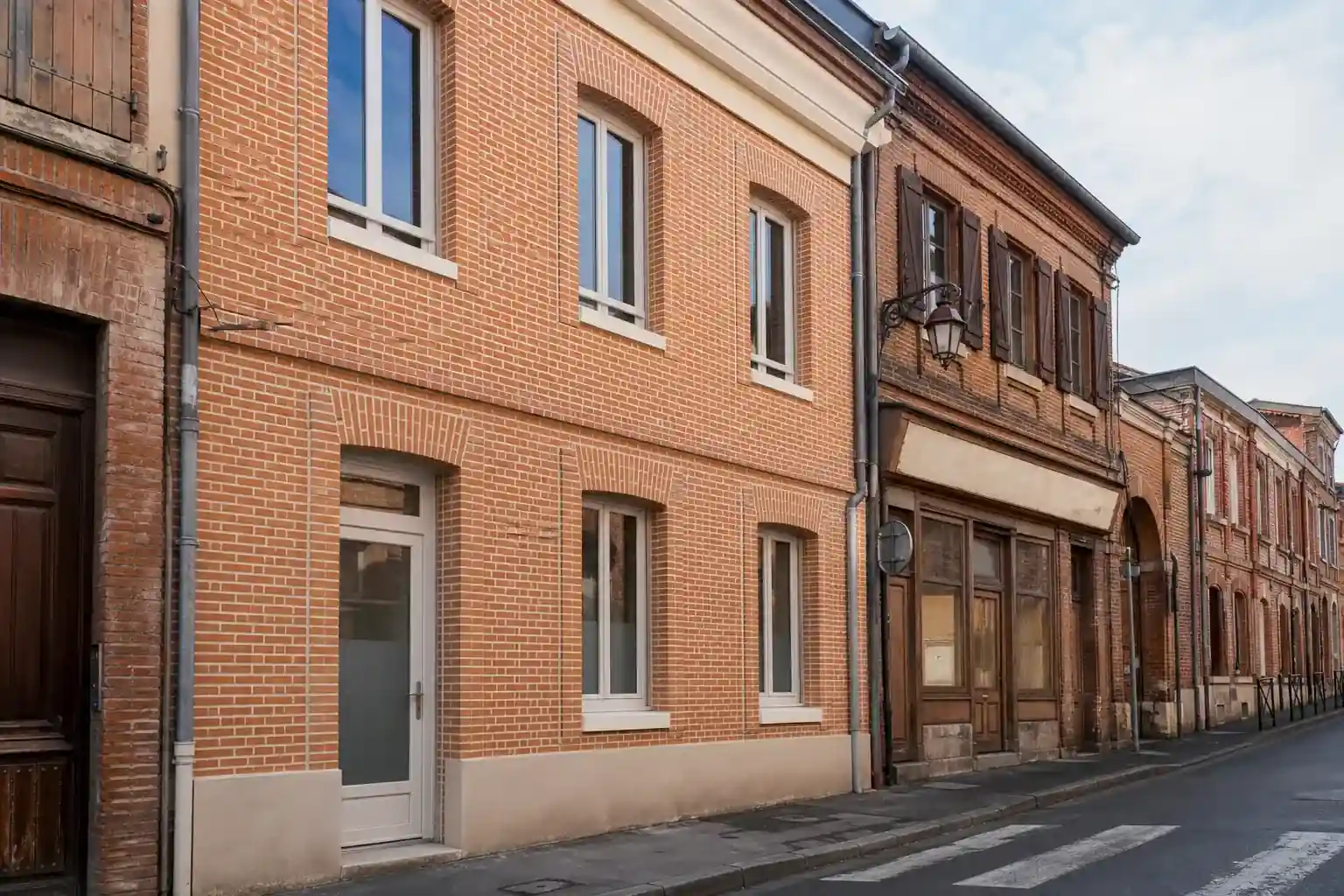 Rue de Carmaux avec maisons de ville en brique, une façade rénovée aux joints nets et menuiseries claires, enseigne de commerce ancienne en fond