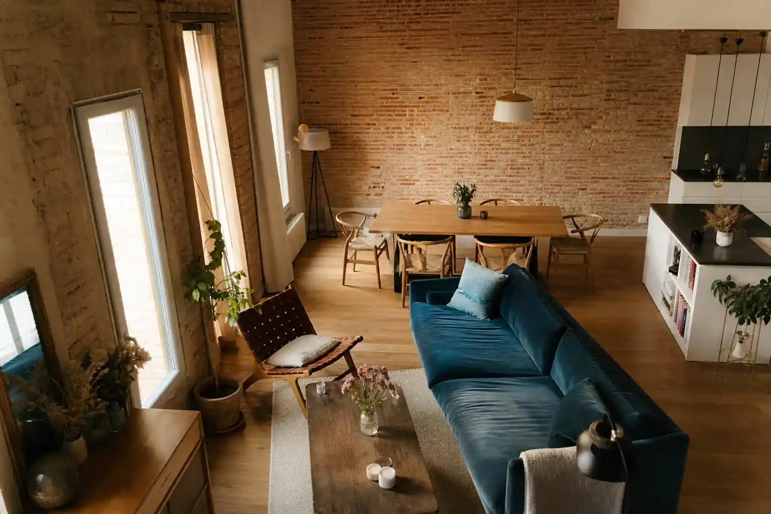 Séjour de maison albigeoise rénovée, grand mur de brique foraine apparente, lumière traversante chaude de fin de journée, cuisine ouverte discrète, vue plongeante légère