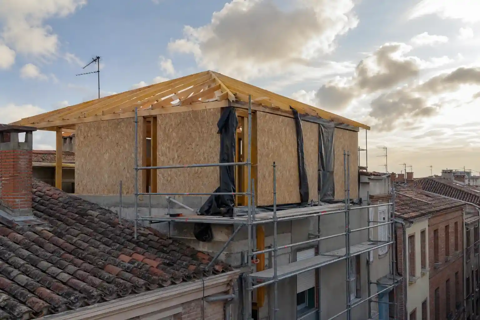 Surélévation en cours de chantier sur une maison de ville albigeoise, charpente bois posée, échafaudage propre, ciel du sud-ouest